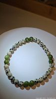 Top view of stretchy bracelet composed of alternating natural green jade and dalmatian jasper beads, laid flat in a circular shape.