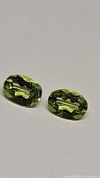 Close-up photo of two oval natural apple green peridots showing faceted cuts and clarity.
