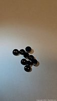 Clear photo of 9 round cabochon black onyx gemstones spaced randomly on a white background showing their polished surface and jet black color.