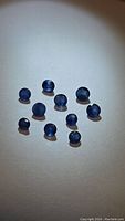 Ten natural round cut blue sapphire gemstones displayed against a light background, showing size variation and blue color.