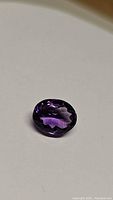 Oval cut deep violet natural Brazilian amethyst gemstone on white background.