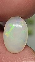Close-up photo of oval-shaped natural Ethiopian opal held between fingers, showing multicolored internal flashes and smooth polished surface.
