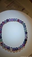 Natural purple rainbow fluorite bead bracelet displayed in circular form on white background. Beads are round and translucent with purple, green, and clear color variations.