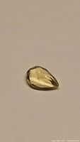 Photo of a pear cut pale yellow lemon citrine gemstone with visible facets and natural inclusions on a plain background.