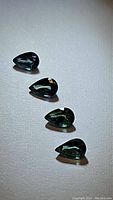 Four pear cut natural sapphires, green-teal-blue hues shown from top side with defined facets under directional lighting on neutral surface.