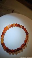 Single stretchy bracelet composed of round 6mm natural red agate beads, arranged in a circular shape, showing warm reddish and orange colors with natural patterns visible on each bead.