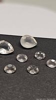 Photo showing 7 natural rose quartz gemstones placed on a dark surface, including two pear-shaped and five round faceted stones, total weight 2.10ct.