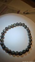 Single natural Yooperlite beaded bracelet arranged in a circle on a white circular surface, showing the speckled pattern of the 6mm beads.