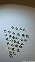 Photo showing over 30 small round faceted Alexandrite gemstones on a white background with lighting that highlights green and yellow color changes.
