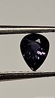 Close-up image of deep purple pear-shaped sapphire held with tweezers, showing faceted cut and color.
