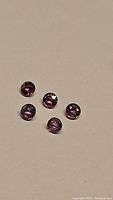 Five loose round cut pink to purple sapphires laid out on a plain background, showing their natural color and cut characteristics.