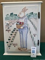 Full front view of the wooden cabinet door showing the painted rabbit holding a basket of vegetables with garden rows labeled.