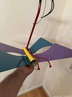 Side angle showing yellow body with red antenna and red connecting pole, teal and purple wings extended horizontally.