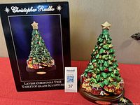 Photo showing the Christmas tree sculpture next to its original branded box on a red cloth surface.