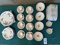 Overview photo showing the complete set laid out, including plates, bowls, cups with saucers, and 8 mugs, all decorated with holly and red berries pattern on cream porcelain.