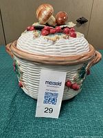 Full view of the ceramic covered container with textured white base, brown rim and handles, and detailed fall-themed lid.