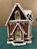Front view of wooden gingerbread house showing brown wood painted to look like gingerbread with white painted icing and colorful candy details on roof and windows
