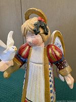 Front view of the wooden angel figurine holding a white dove on the right hand, showing detailed painted red robe, golden halo, and smiling face.