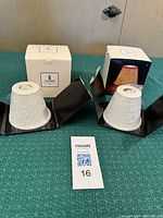 Two matte white porcelain Lladro Magic Light lithophanes with lace engraving displayed with original boxes on a green surface.