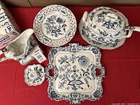 Top-down group shot showing square platter, round pierced plate compote, soup tureen with platter and ladle, gravy boat and candlestick on red background