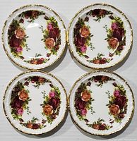 Four Royal Albert Old Country Roses butter pat dishes arranged side by side showing floral pattern and gold trim.
