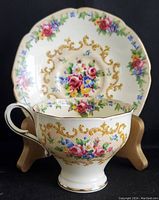 Front angled view of teacup with saucer in background showing floral and gold scroll designs.