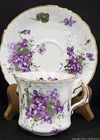 Tea cup and saucer displayed together on wooden stands, showing full floral pattern and gold accents.
