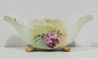 Side view of footed mint dish showing floral hand painted design on curved edge and base with golden feet.