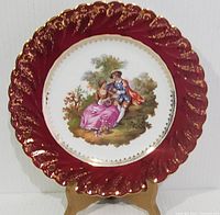Full view of the Limoges France decorative plate with red and gold ornate border and central couple portrait scene.