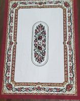 Full view of tablecloth showing central oval poinsettia motif and decorative borders on white and red background.
