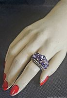 Ring shown on mannequin hand with red nail polish to display size and fit.