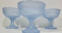 Front view of four frosted powder blue Luminarc dessert bowls with raised fruit design, showing color and texture