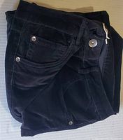 Folded black corduroy pants showing front pocket and metal button