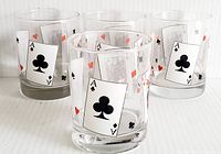 Photo showing front view of four vintage low ball glasses with playing card images, focusing on Ace of Clubs card design.