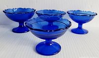 Four blue glass footed dessert or sherbet bowls arranged standing upright, showing scalloped rims and pedestal bases.