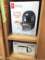 Photo of boxed President's Choice Compact Air Fryer and Braun Aromaster 12-cup glass jug on wooden shelf.