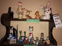 Overview of shelf with multiple cat and bunny figurines of various sizes and materials