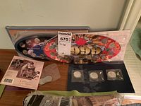 View of two Millennium coin display cases with multiple coins, Royal keepsake booklet booklet with Queen Elizabeth II portrait cover, and small plastic bag of additional coins.