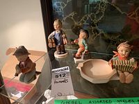 Four porcelain Hummel figurines displayed in glass cabinet variety of boys holding items