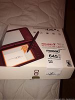 Original box with burgundy Nintendo DS XL image and text describing included features and pre-installed games.