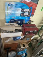 Lot contents showing battery charger, car vacuum, and packaging for car wash soap kit, visible cords and power plug, multiple items placed on shelving unit