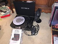 Black Victrola Bluetooth turntable VSC-550BT in an open carry case with a white record platter and two wired headphones beside it, one on a stand.