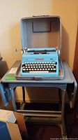 Typewriter in open carrying case on metal drop-leaf cart