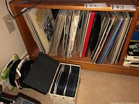 Wide view of vinyl LP records on wooden shelf and box with 45 RPM singles on floor.