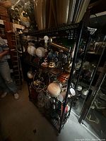 Black wire rolling shelf with four shelves showing various items placed on it for context, shelving unit black metal with rolling wheels.