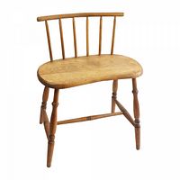 Front view of farmhouse wooden chair showing spindle backrest, contoured seat, and turned legs.
