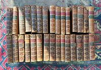 Two rows of 27 leather-bound books with gilt-decorated spines on patterned rug