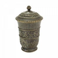 Photo of metal covered jar with intricate embossed floral and ornamental patterns in a dark bronze finish.