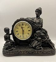 Front view of the detailed bronze-tone figurine clock showing woman and two children around clock face with Roman numerals.