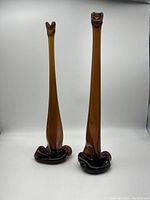 Photo of two tall brown stretched glass vases with ruffled flared bases against a white background.